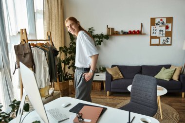 Genç bir adam, bitkiler ve modern dekorlarla çevrili güneşli bir odada giyinirken gülümsüyor..