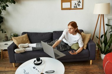 The young man is lounging on a couch, focused on his laptop with a relaxed demeanor. clipart