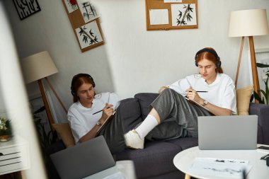 Focused young man sketches in cozy home studio while listening to music with enthusiasm. clipart