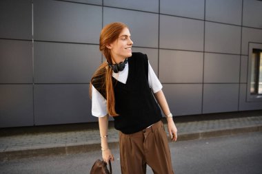 Genç bir adam modern bir şehir ortamında neşeli bir gülümseme ile gelişigüzel giyinmiş bir anın tadını çıkarıyor..