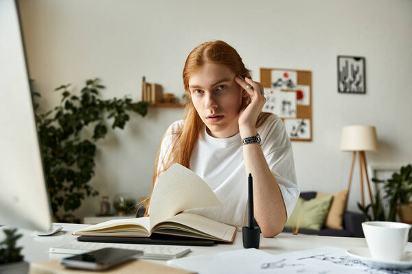 Молодой человек с длинными волосами задумчиво смотрит на открытую книгу в солнечном, привлекательном кабинете.