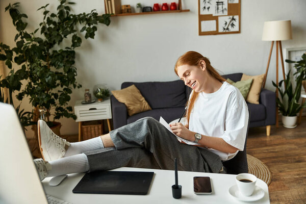 A young man is seated comfortably, writing in a notebook with a pencil and a cup of coffee nearby.