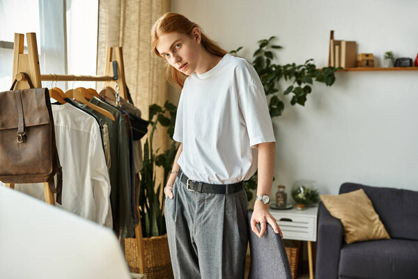 Стильный молодой человек задумчиво позирует в хорошо оформленной комнате, наполненной одеждой и растениями..