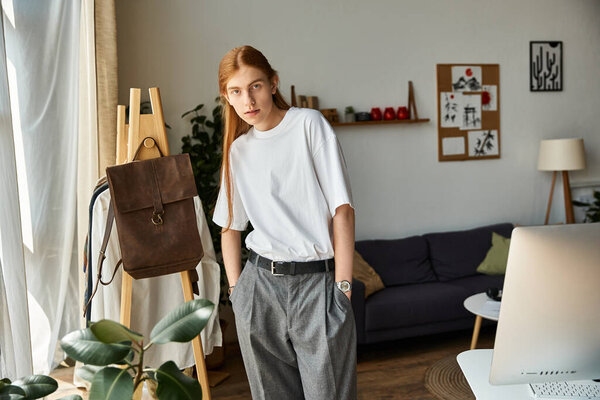 Молодой человек в стильной одежде небрежно наклоняется в современном жилом пространстве, украшенном искусством.