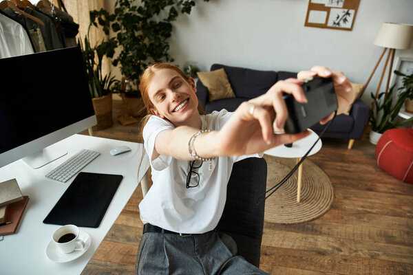 A young man smiles brightly while taking a selfie in a warm, inviting workspace.