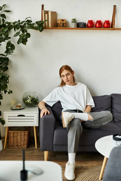 A young man sits comfortably on a sofa, surrounded by modern decor and greenery.