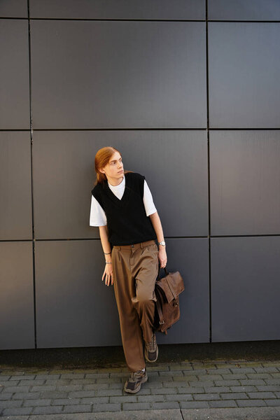 Молодой человек, одетый в повседневный, но модный наряд уверенно позирует против гладкой геометрии.