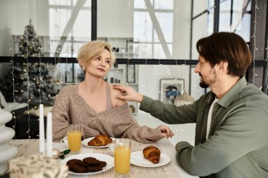 Bir çift, yemek masasında kahvaltı ikramıyla dolu hassas bir anı paylaşıyor..