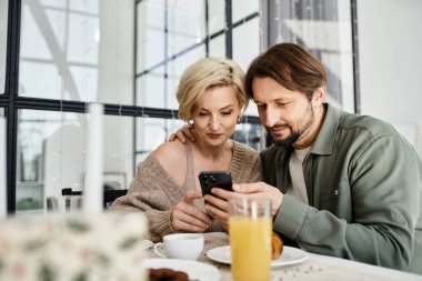 Bir çift evde oturup kahvaltıda kahkaha ve sıcaklığı ve akıllı telefonu paylaşıyor..