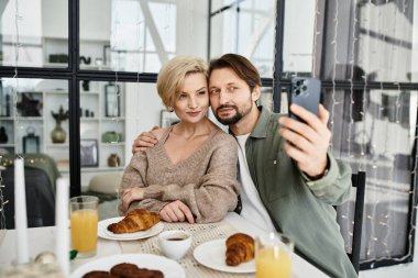 Çift evde sıcak bir kahvaltı sırasında selfie çekerken mutlu bir şekilde gülümser..