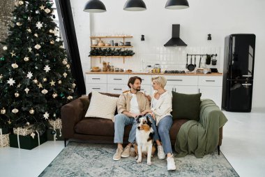 Bir çift rahat bir kanepede rahatlar, neşeli bir ortamda köpekleriyle gülümsemelerini paylaşırlar..