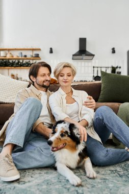 Neşeli bir çift yerde rahatlar, köpekleri yakınlarda oynarken kahkahalarını ve sevgilerini paylaşırlar..