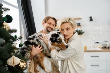 Mutlu bir çift neşeli köpeklerini kucaklarken şenlik zamanlarında evlerinin sıcaklığının tadını çıkarıyor..