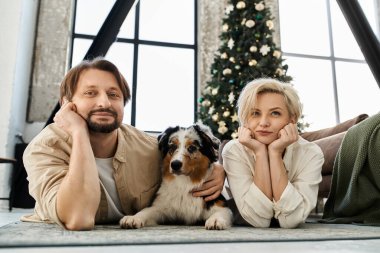 Neşeli bir çift köpekleriyle yerde rahatlar, evde sıcaklığı ve mutluluğu yakalarlar..