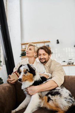 Bir çift kanepede sevimli köpekleri ile birlikte rahatlar, gülümsemelerini ve sıcaklığını evlerinde paylaşırlar..