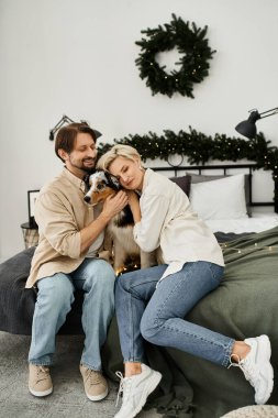 Bir çift evde sıcak bir anın tadını çıkarıyor. Şenlikli dekorlar ve hafif ışıklandırmalar arasında köpeklerine sarılıyorlar..