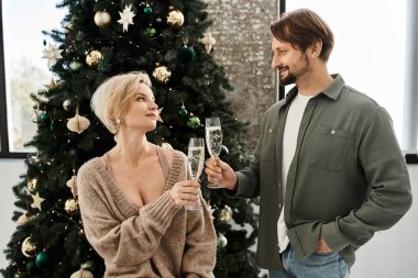 Bir çift, şenlikli Noel ağacının yanında otururken birlikte köpüklü içeceklerden zevk alır..