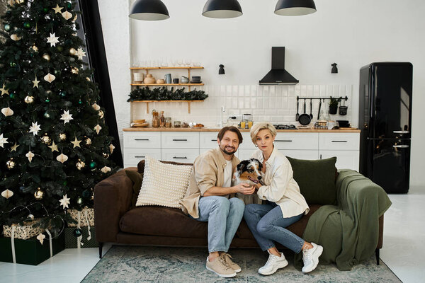 Пара наслаждается теплым моментом дома со своей собакой, в окружении праздничных украшений.