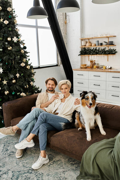 A couple relaxes on a couch, enjoying drinks with their dog beside them during the holidays.