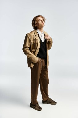 Yakışıklı genç bir adam şık bir sonbahar kıyafetinin içinde duruyor, bir stüdyoda zarafet saçıyor..