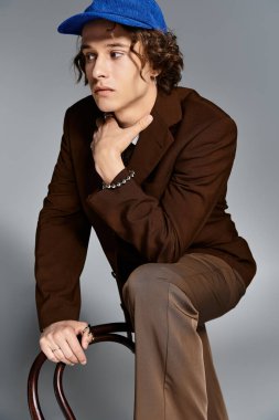 Kahverengi takım elbiseli ve mavi beysbol şapkalı şık bir genç, eşsiz yeteneğini bir sanat stüdyosunda sergiliyor..