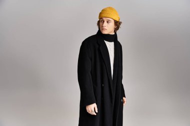 A handsome young man showcases a chic black coat and a bright yellow beanie in a modern studio setting. clipart