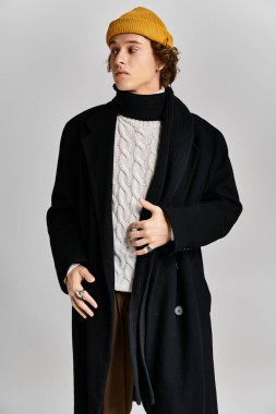 Şık bir genç adam, tarzını siyah bir ceket ve sarı bir bereyle sergiliyor. Stüdyoya güveni tam..