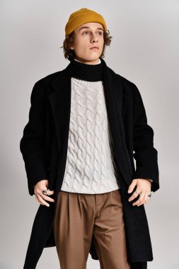 Şık bir genç adam şık bir stüdyoda sarı bereli ve siyah ceketli modaya uygun kıyafetlerini sergiliyor..