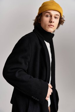 Genç bir adam, stüdyoda yaratıcı bir şekilde poz veren siyah ceketli ve sarı bereli bir adama güveniyor..