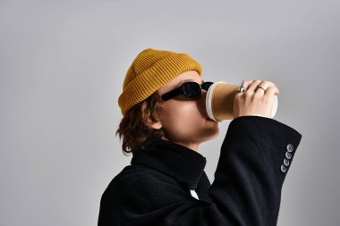 Yakışıklı genç bir adam, şık siyah bir ceket ve parlak sarı bir şapka giyerken kahveyi yudumluyor..