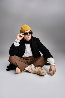 Yakışıklı genç bir adam, stüdyoda dinlenirken kendine has tarzını siyah bir ceket ve sarı bir bereyle sergiliyor..