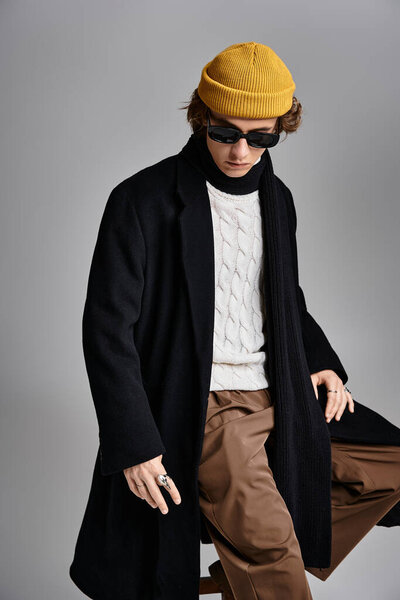 A handsome young man showcases his fashionable style in a black coat and vibrant yellow beanie in the studio.