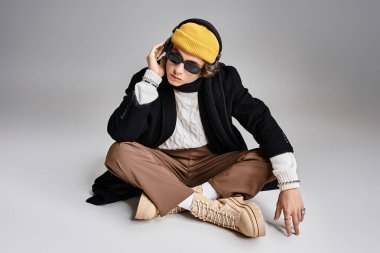 Siyah paltolu ve sarı bereli yakışıklı genç bir adam zarif bir şekilde oturuyor ve stüdyoda eşsiz bir stil sergiliyor..