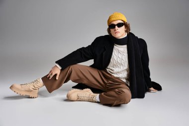 Modaya uygun genç bir adam zarif bir şekilde siyah bir ceket ve sarı bereyle oturuyor ve eşsiz tarzını sergiliyor..