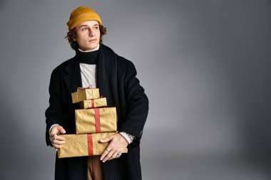 A fashionable young man with a yellow beanie balances beautifully wrapped gifts in a studio setting. clipart