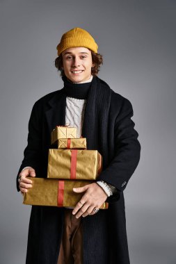 Siyah ceketli ve sarı bereli yakışıklı genç bir adam güzel paketlenmiş hediyeler tutar..