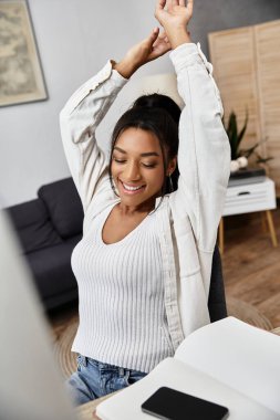 The woman stretches happily while studying at her home, radiating positivity and focus. clipart