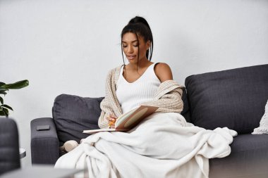 A beautiful young woman engages in remote studying on her couch, immersed in her books. clipart