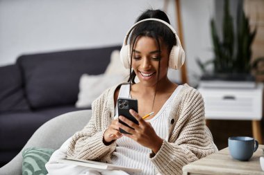 Genç bir kadın rahat bir ortamda, telefonuna gülümseyerek ders çalışmaktan hoşlanır..
