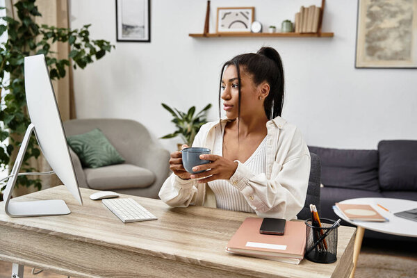 Сосредоточенная молодая женщина учится онлайн, держа горячую чашку кофе в своем домашнем офисе в Серене.