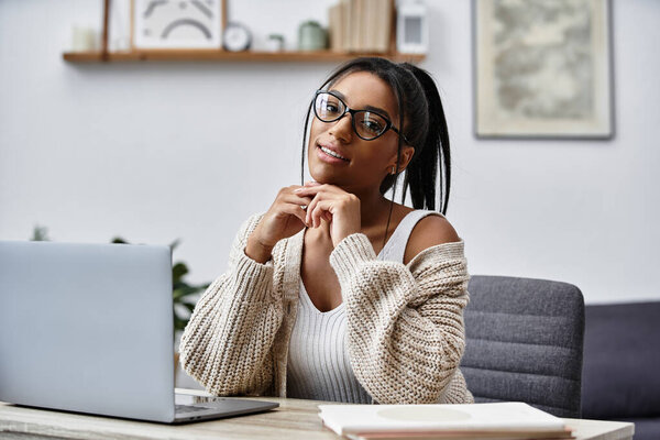 The young woman smiles while studying at home, dressed comfortably and surrounded by books.