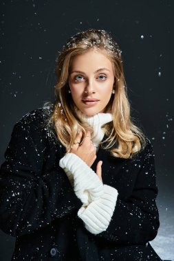 A beautiful young woman with blonde hair enjoys a moment as snowflakes softly fall around her.