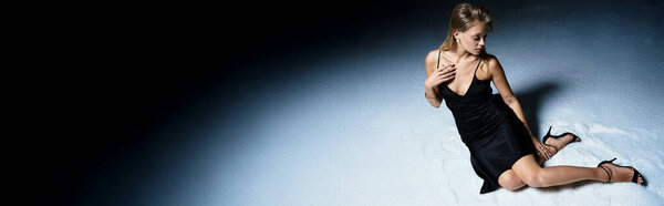 A beautiful young woman in a chic black dress sits gracefully, showcasing elegance and poise.