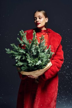 A beautiful young woman dressed in vibrant red holds a fresh greenery arrangement while posing. clipart