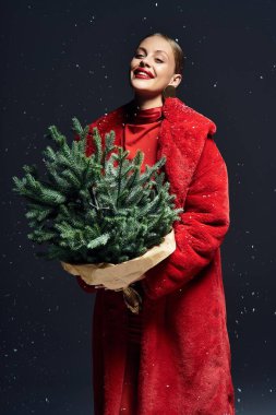 The woman radiates joy as she embraces a lush winter tree, dressed in warm red attire. clipart