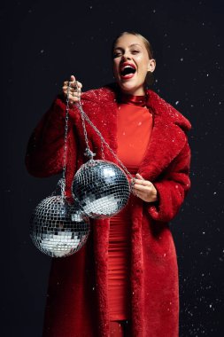 Enthusiastic young woman with a radiant smile showcases disco balls in a festive setting clipart