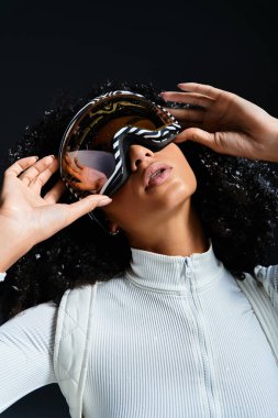 Şık bir kayak takımı giymiş güzel bir Afro-Amerikalı kadın, kış tarzını vurgulayarak kendine güvenerek poz veriyor..