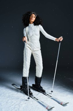 A beautiful brunette woman in a sleek ski suit elegantly poses while highlighting winter fashion indoors. clipart