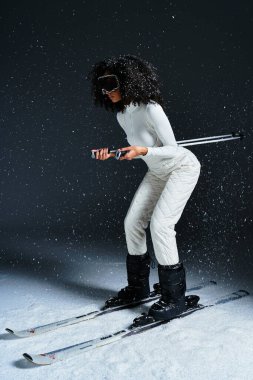 A stylish brunette African American woman models a chic ski suit in a dynamic studio setting. clipart