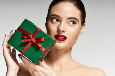 Bu çarpıcı kadın elinde kırmızı kurdeleyle yeşil bir hediye tutarken gülümsüyor..